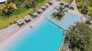 Luftaufnahme eines Resorts mit großem Swimmingpool, Liegestühlen und einer kleinen Insel mit einer Palme.