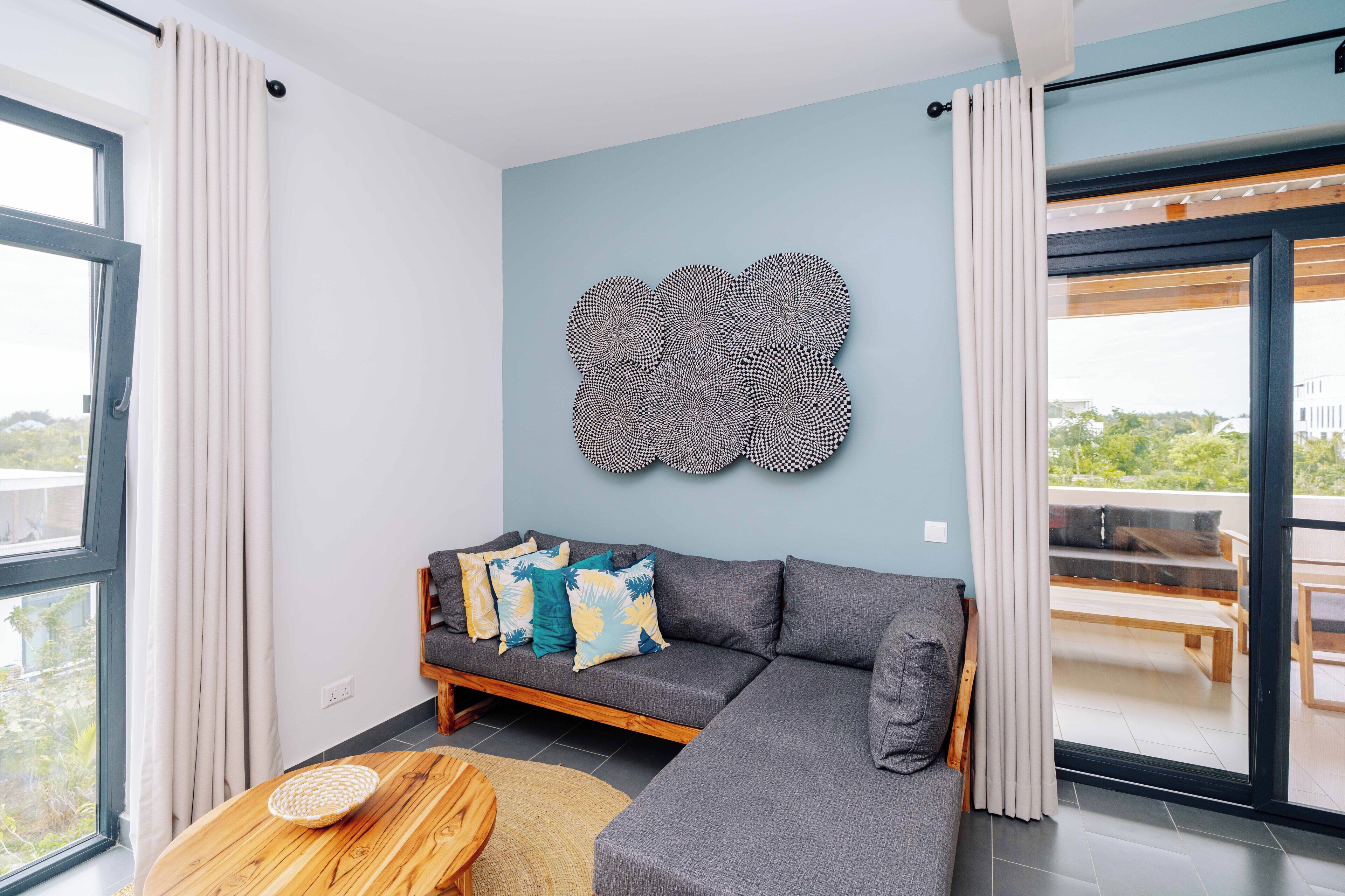 Una sala moderna con un sofá seccional gris, una mesa de centro redonda de madera y una obra de arte en la pared.