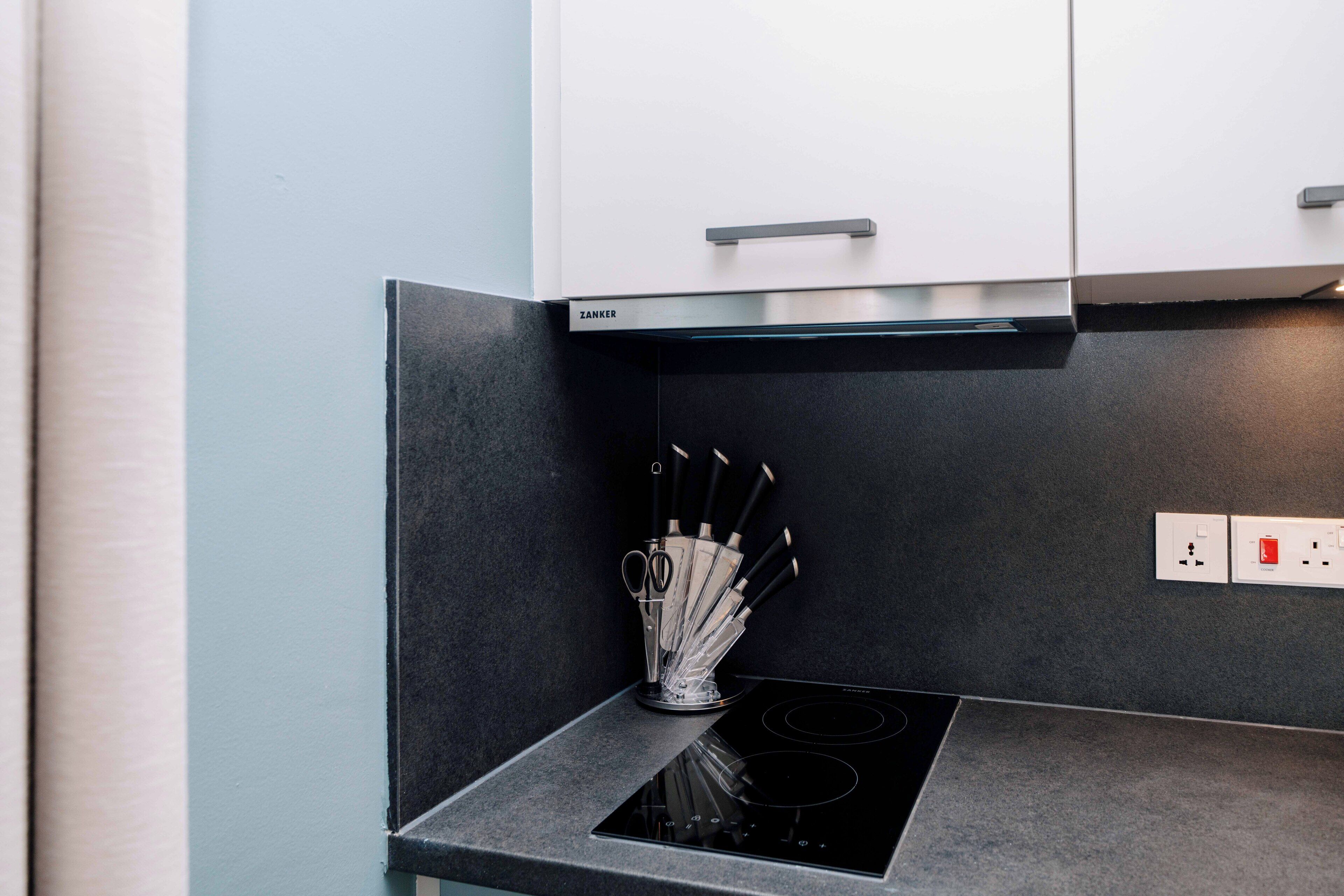 A kitchen with a black countertop, a stove, and a knife holder.