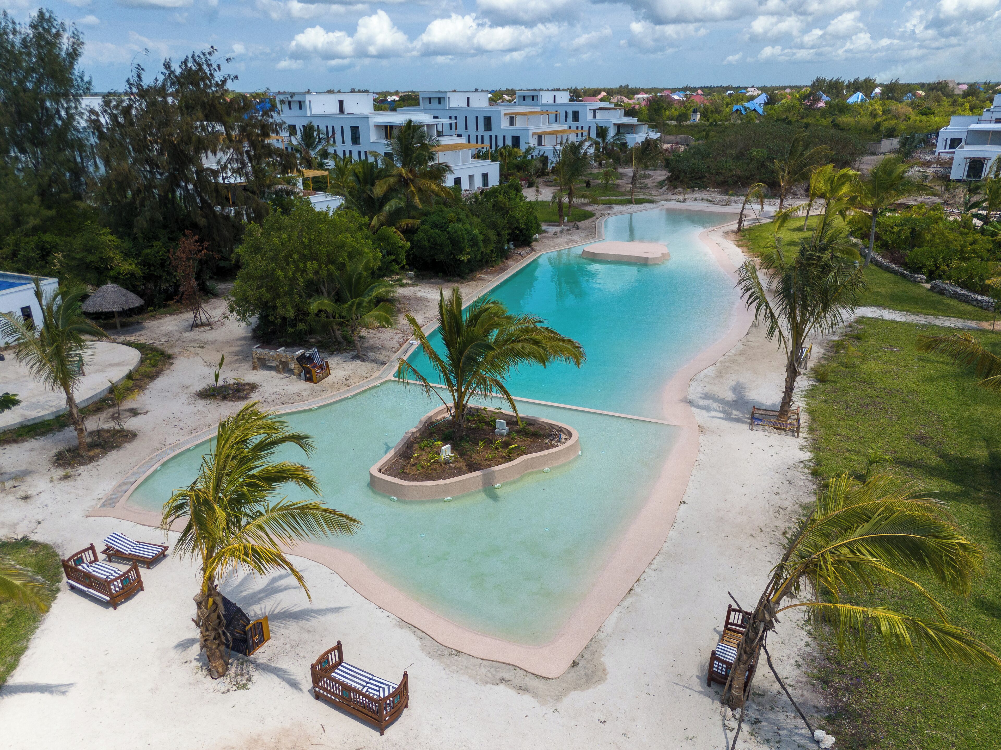 Un resort con una piscina grande, palmeras y sillas de playa.