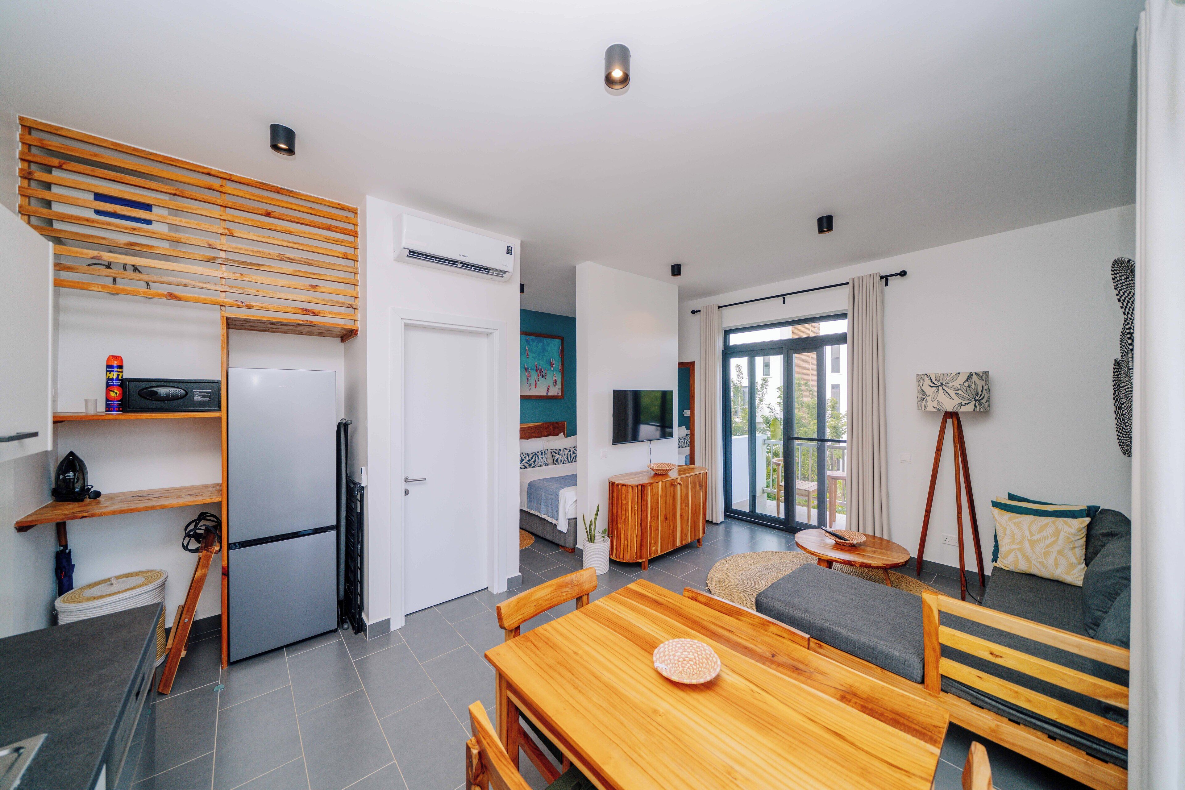 A modern kitchen with a built-in refrigerator, wooden shelves, and a dining area with a wooden table and chairs.