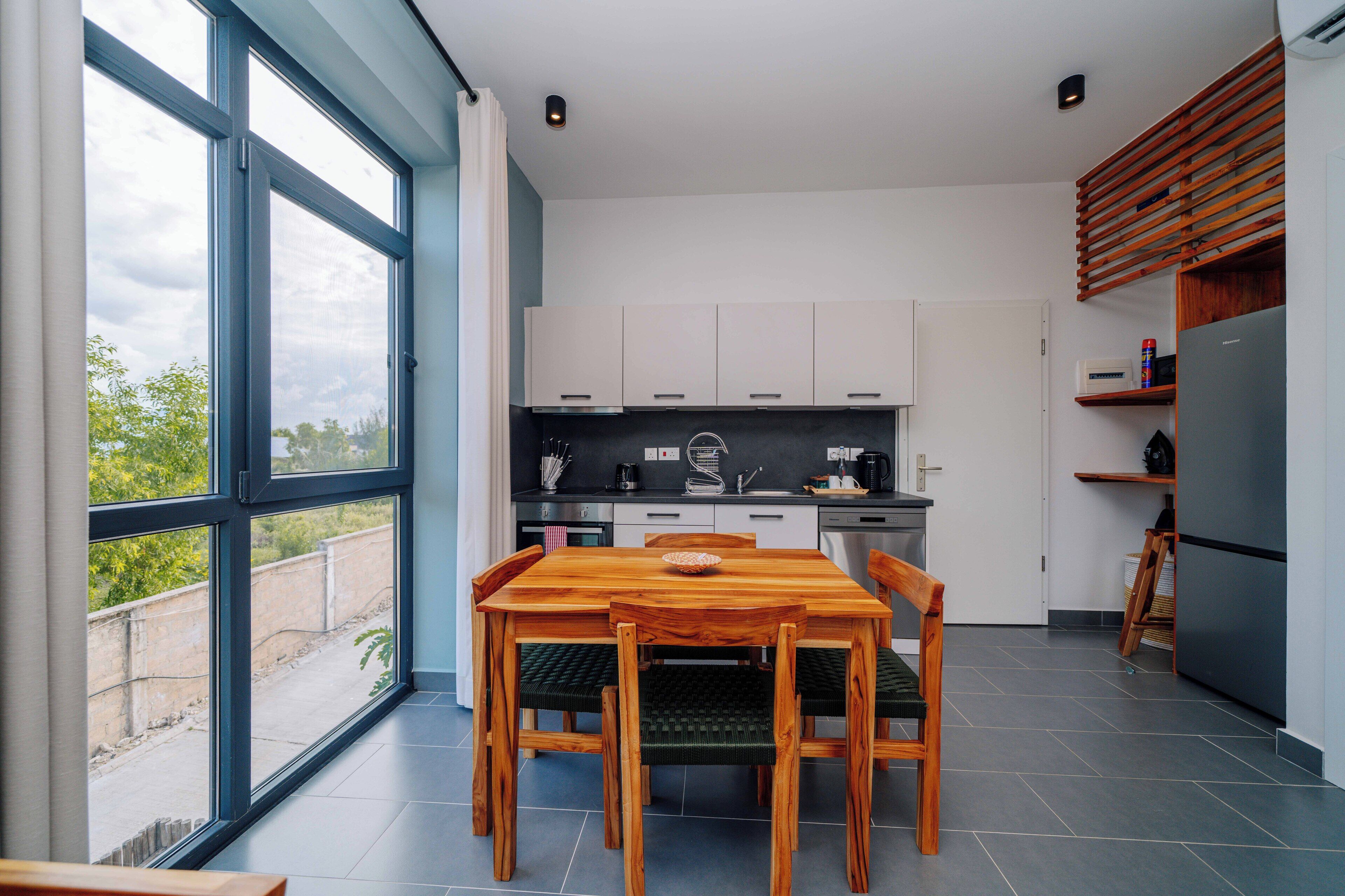 A modern kitchen with a dining table and chairs, large windows, and a built-in oven.