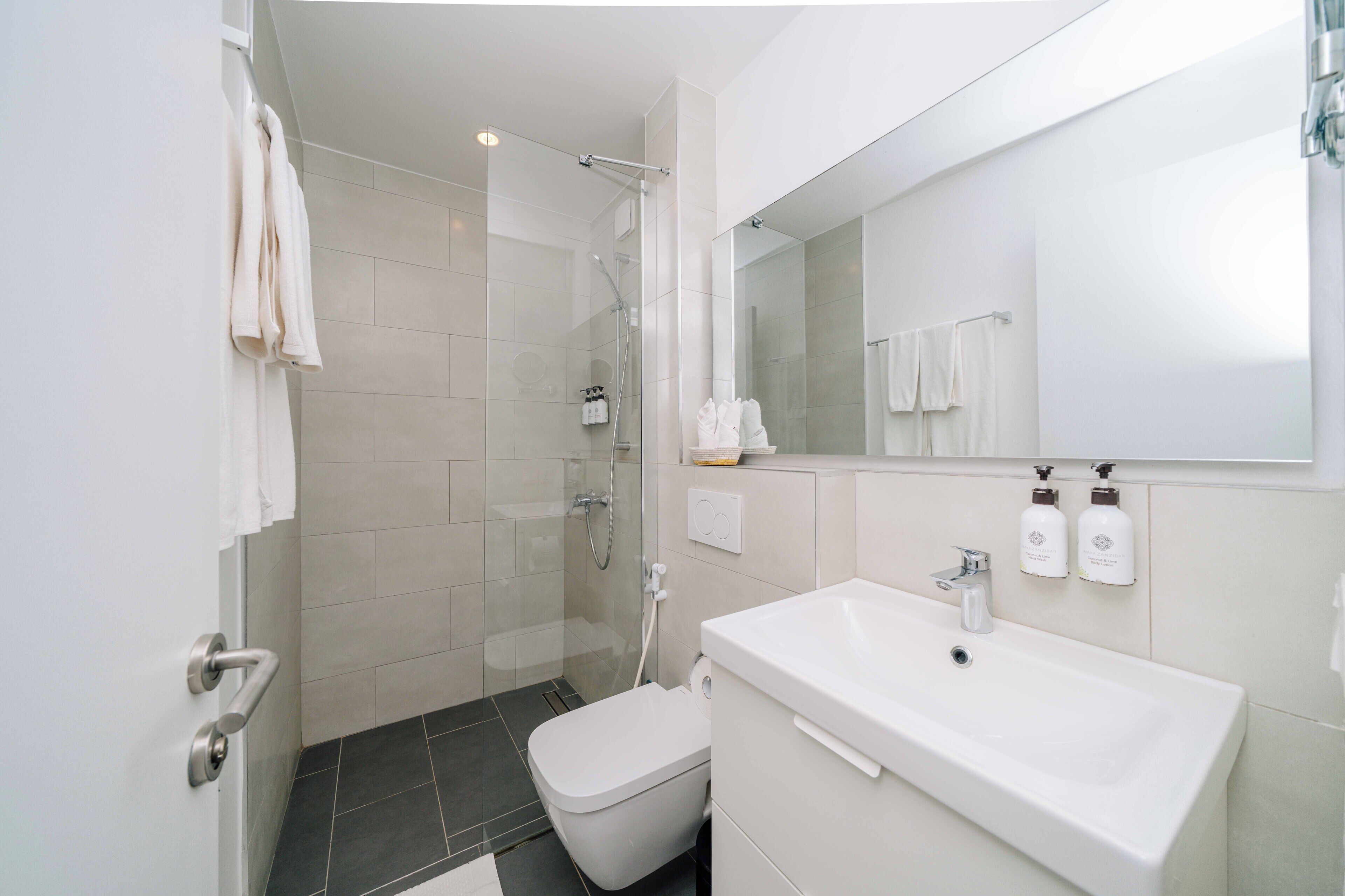 Une salle de bain moderne avec une douche à parois de verre, un lavabo blanc doté de deux distributeurs de savon et des toilettes.