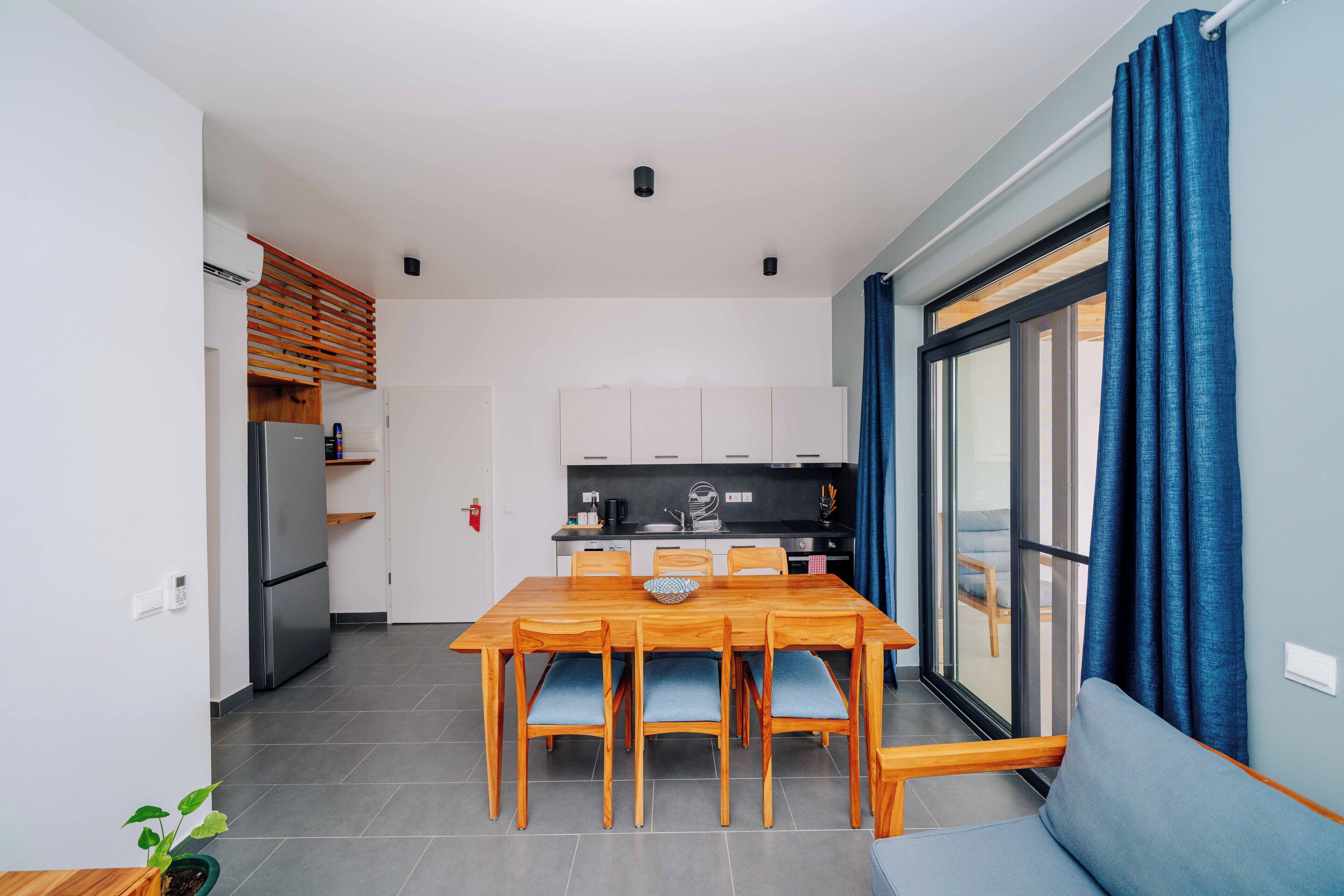 Una cocina moderna con armarios blancos, un refrigerador de acero inoxidable y un comedor con una mesa de madera y sillas azules.