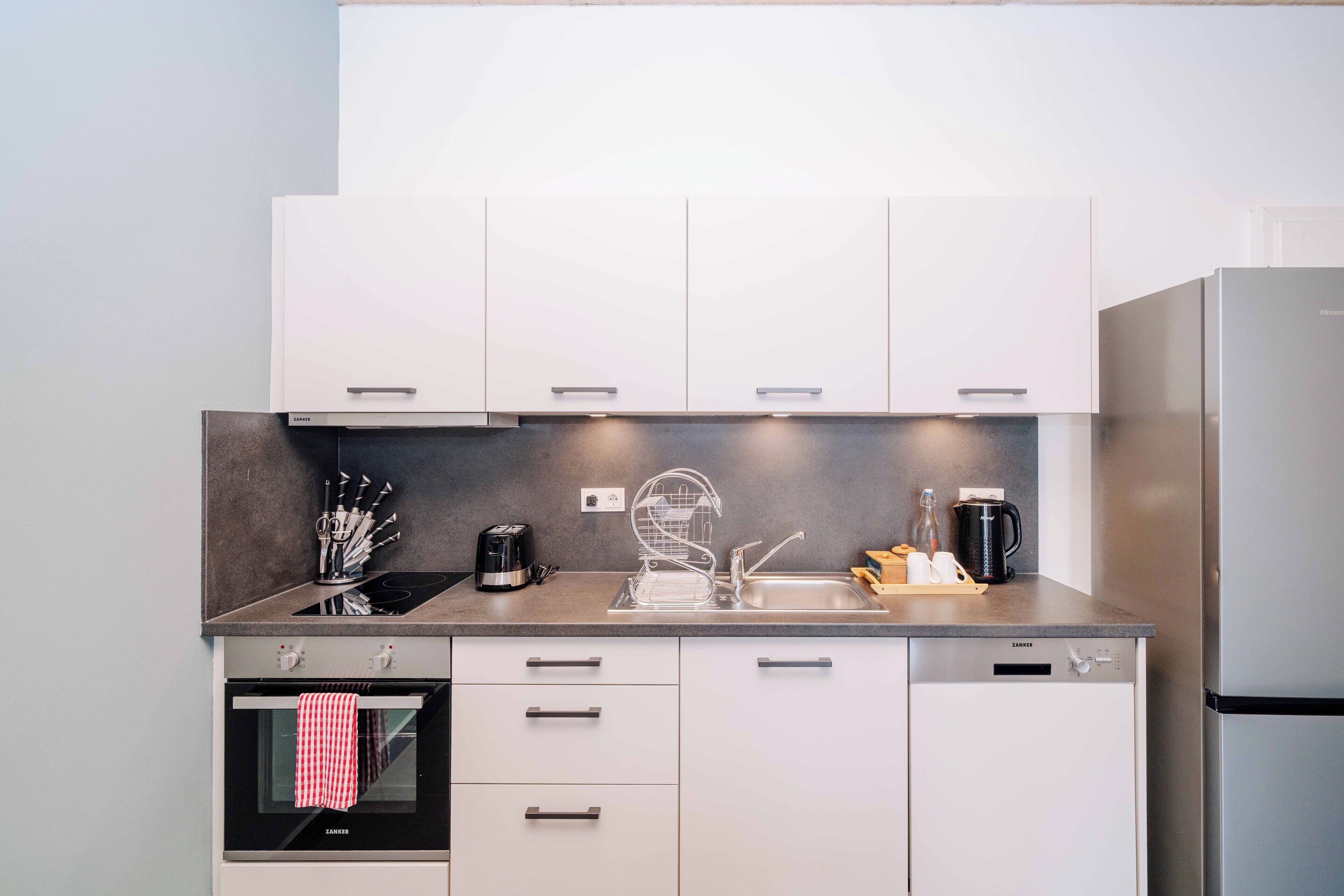 A modern kitchen with white cabinets, a stainless steel refrigerator, a built-in oven, and a coffee maker on the counter.