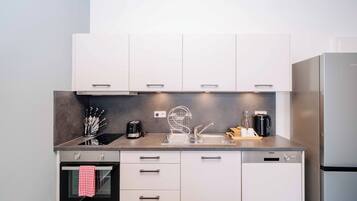 Una cocina moderna con armarios blancos, un refrigerador de acero inoxidable, un horno empotrado y una cafetera sobre la encimera.