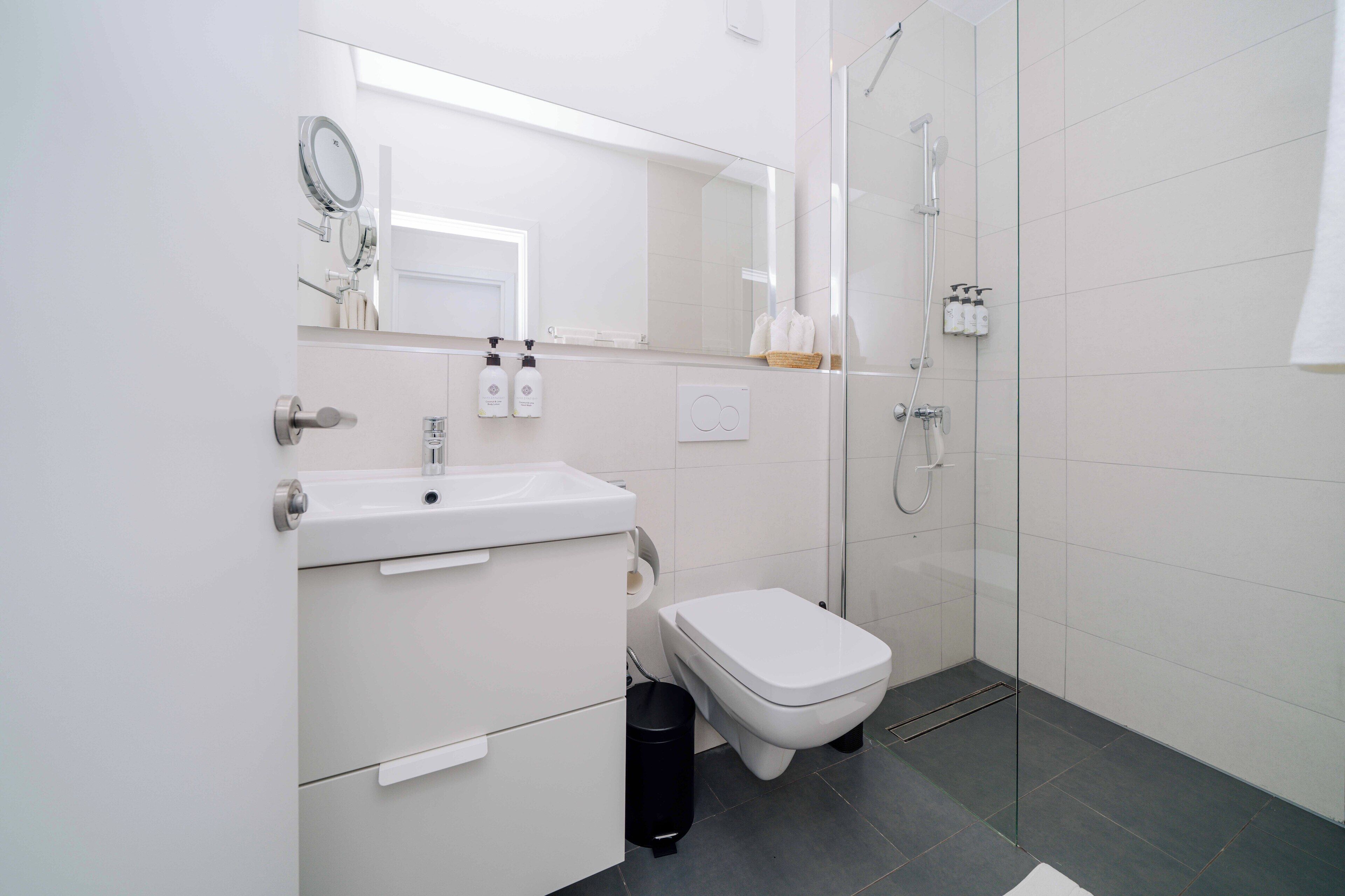 A modern bathroom with a white sink, toilet, and glass-enclosed shower.