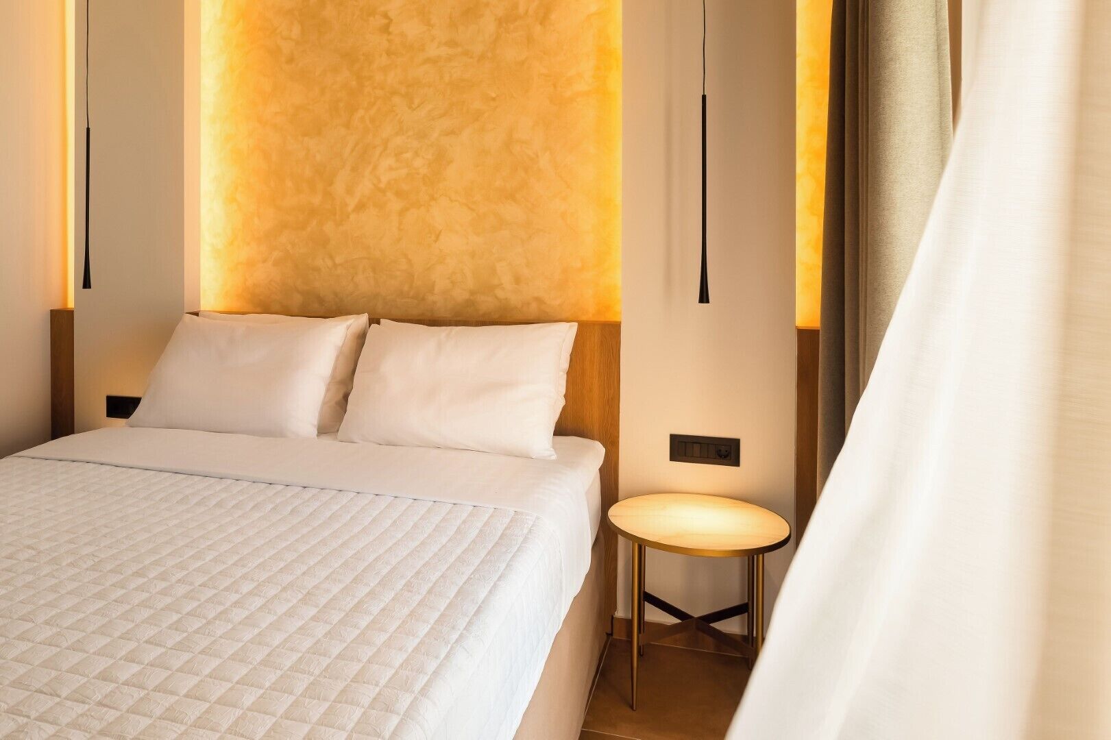Habitació d'hotel amb un llit, una tauleta de nit i una làmpada de paret.