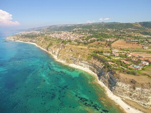 An aerial view of a coastal town with a clear coastline, residential areas, and a beach. - Le Playe Village (Ricadi)