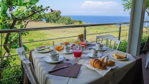 Una tavola apparecchiata per la colazione con vista sul mare, con piatti di cibo, tazze e un bicchiere di succo di frutta.