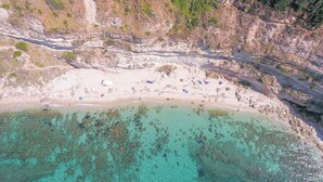 Vista aerea di una spiaggia con acque cristalline color turchese, una battigia sabbiosa e alcuni ombrelloni sparsi.