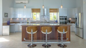 Una cocina moderna con una isla central, taburetes de bar, electrodomésticos de acero inoxidable y ventanas amplias.