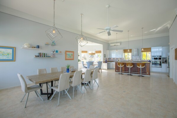 A spacious dining area with a wooden table and chairs, a kitchen with a bar, and a ceiling fan. - Spacious, Modern 6-Bedroom Villa in Lovely Dawn Beach (Philipburg)