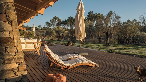 A wooden deck with lounge chairs and umbrellas, surrounded by trees and a stone wall. - TEIMA Alentejo SW (Odemira)