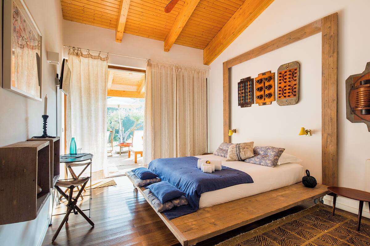 A bedroom with a wooden bed, a desk, and a chair. There is a window with curtains, a lamp, and a wall-mounted light fixture.