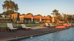 A poolside area with lounge chairs and umbrellas, a stone building with a red roof, and a clear sky. - TEIMA Alentejo SW (Odemira)