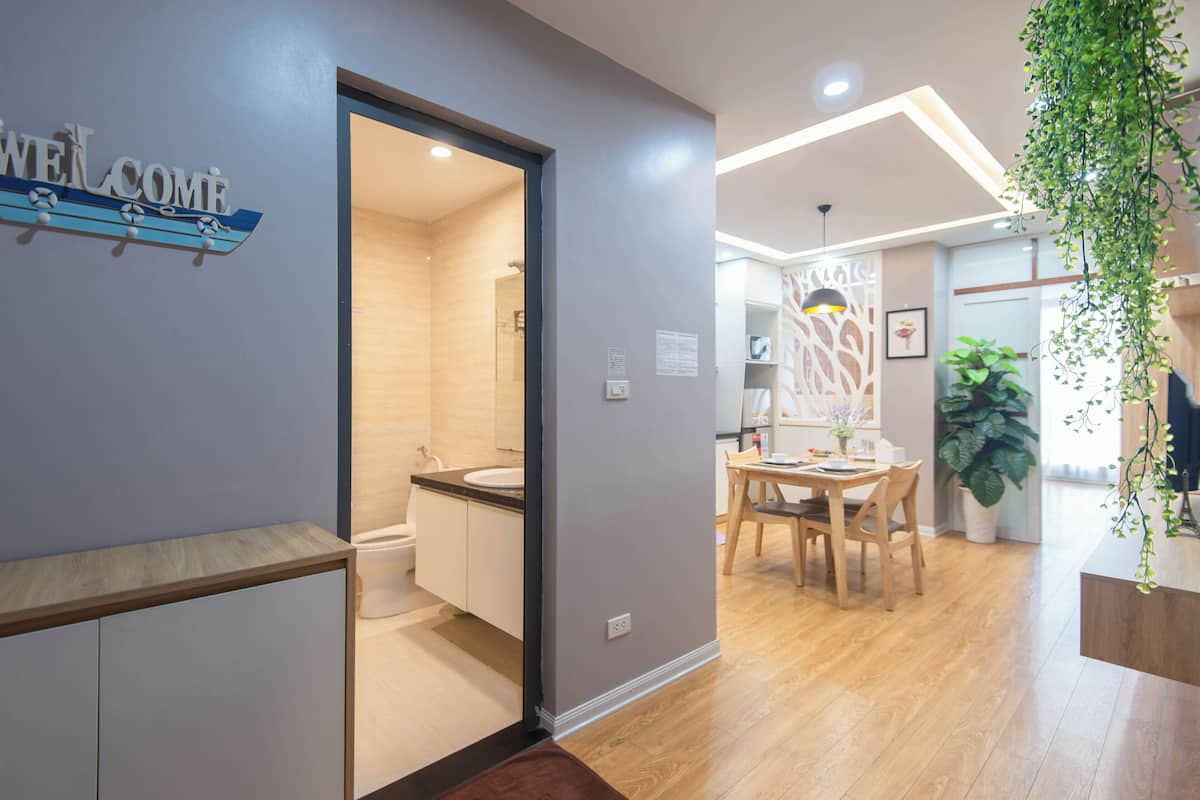 Ein modernes Hotelzimmer mit Holzboden, einem Badezimmer mit Waschbecken und Toilette, einem Essbereich mit Tisch und Stühlen sowie einer hängenden Pflanze.