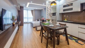 Una habitación de hotel moderna con zona de comedor, kitchenette y un amplio ventanal con cortinas.