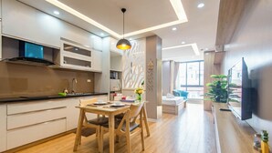 Una cocina moderna con suelo de madera, un comedor con mesa y sillas, y una sala de estar con sofá y televisor.