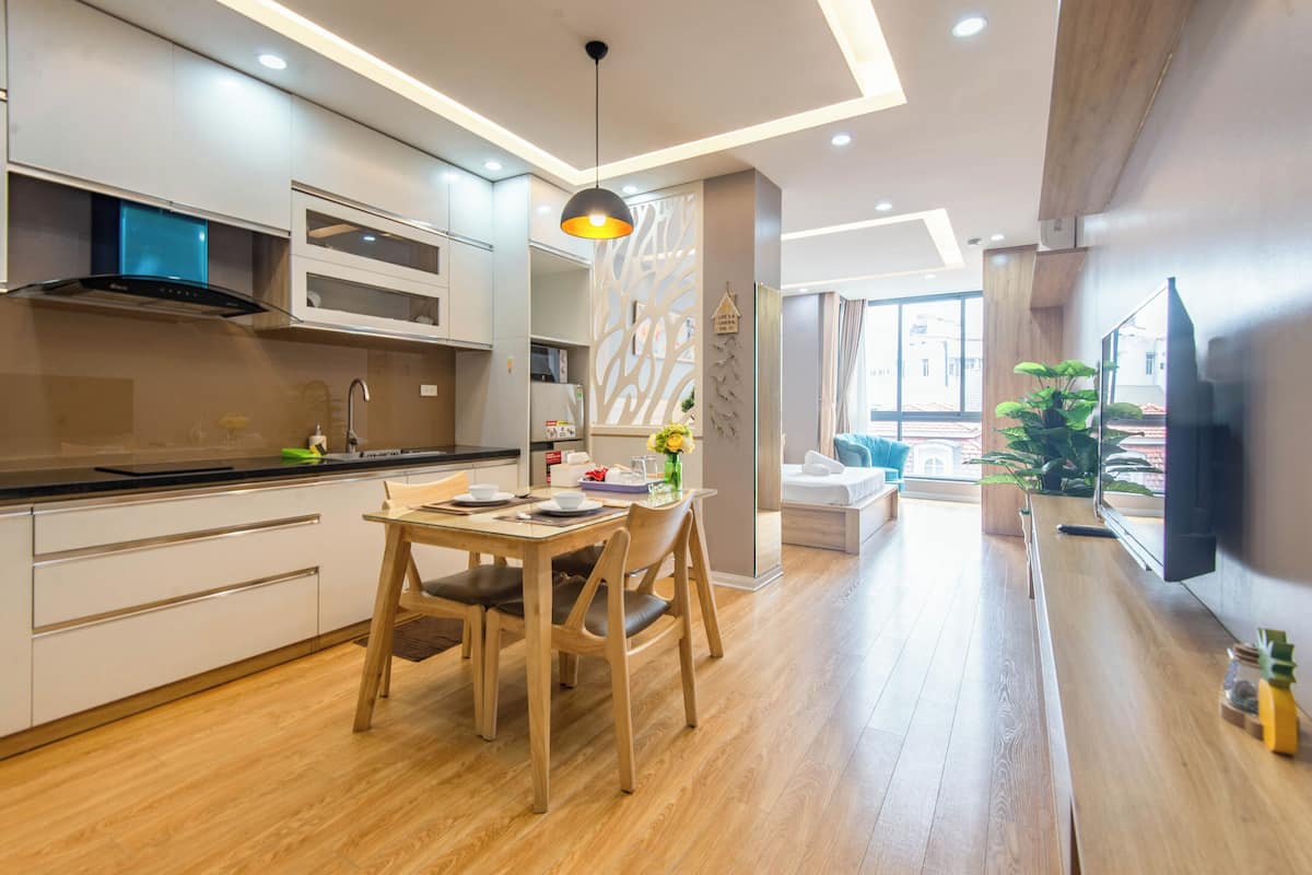 Eine moderne Küche mit Holzboden, einem Essbereich mit Tisch und Stühlen sowie einem Wohnbereich mit Sofa und Fernseher.