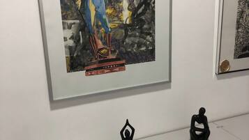 A framed artwork on a wall, a small black sculpture on a counter, and a grey cabinet below.