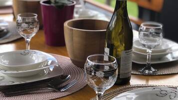 Une table à manger dressée avec des assiettes, des couverts et des verres à vin, une bouteille de vin et une plante en pot en arrière-plan.