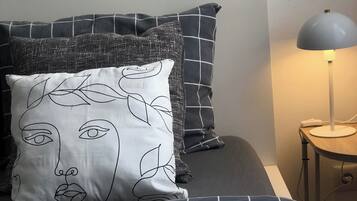 Una cama con un almohadón estampado, una lámpara e interruptor de pared.