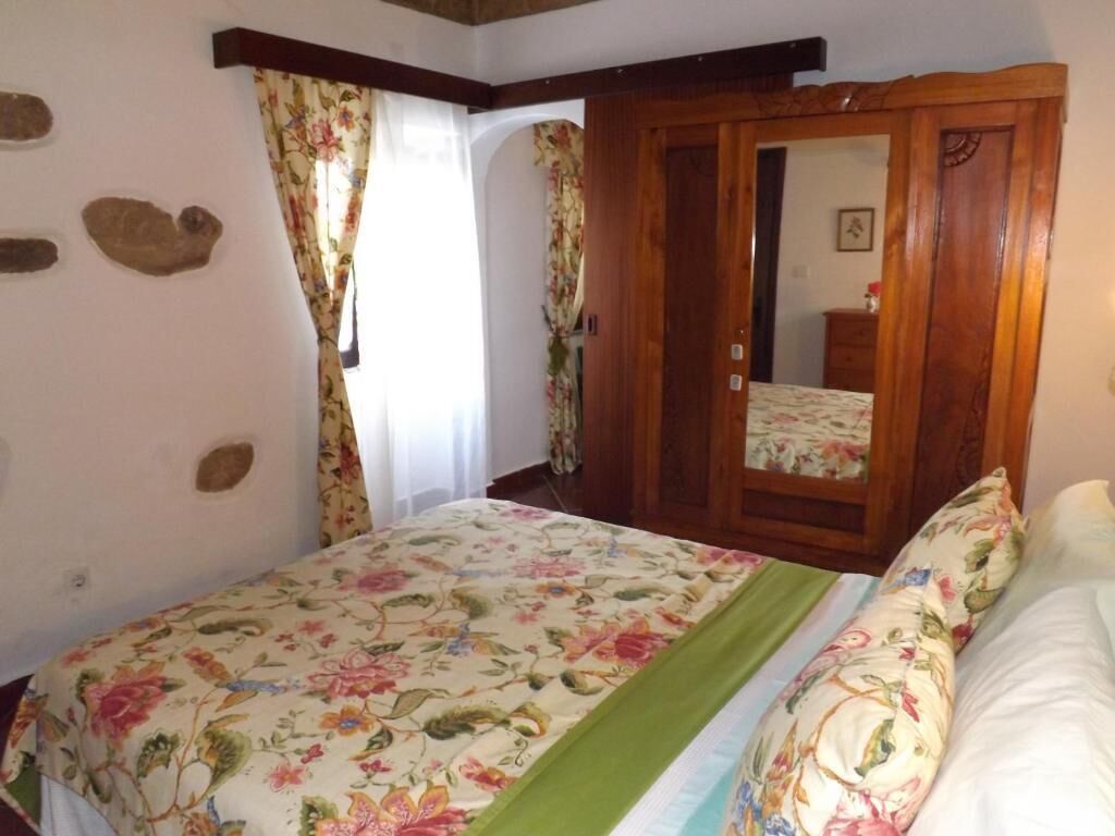Un dormitorio con cama, cortinas florales, un armario de madera y una pared de piedra.