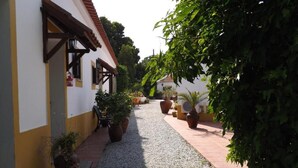 A narrow alleyway with a gravel path, flanked by buildings with yellow and white walls, and potted plants. - Quinta do Xarrama (Évora)
