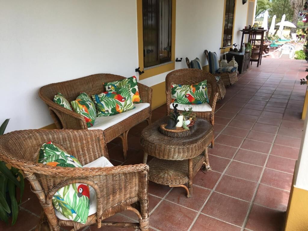 Wicker furniture with tropical leaf-pattern cushions, a tiled floor, and a yellow wall.