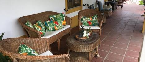 Wicker furniture with tropical leaf-pattern cushions, a tiled floor, and a yellow wall.