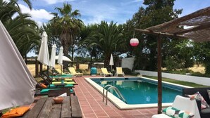 A pool area with lounge chairs, a wooden table, and umbrellas. - Quinta do Xarrama (Évora)