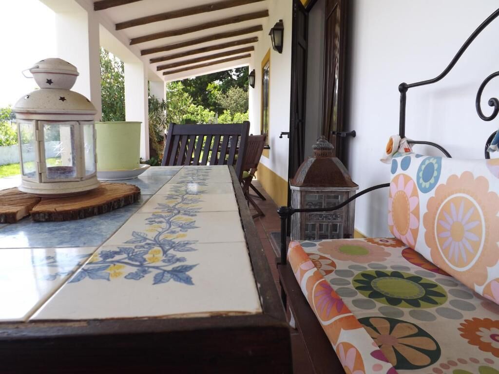 A covered patio with a wooden table, a bench, and a colorful sofa.