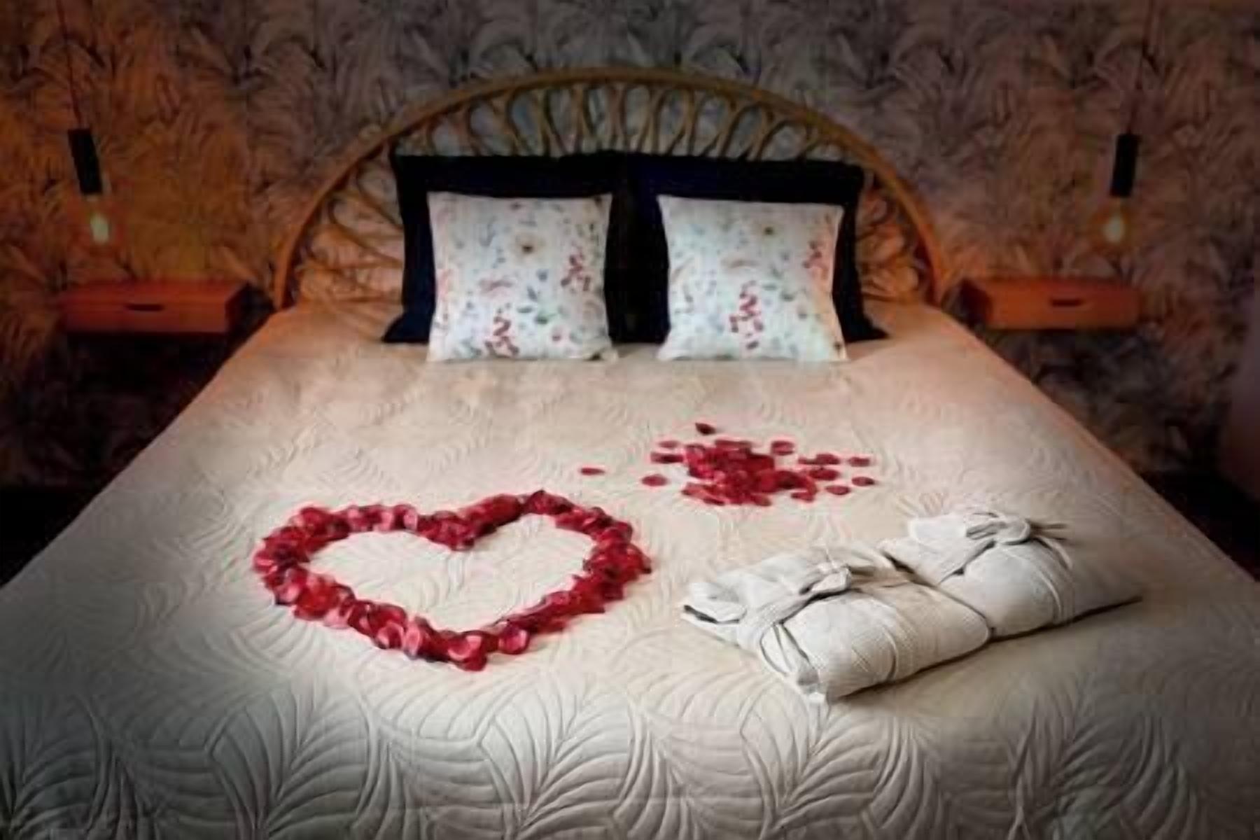 Un lit décoré de pétales de roses disposés en forme de cœur et sur lequel est posée une serviette soigneusement pliée.