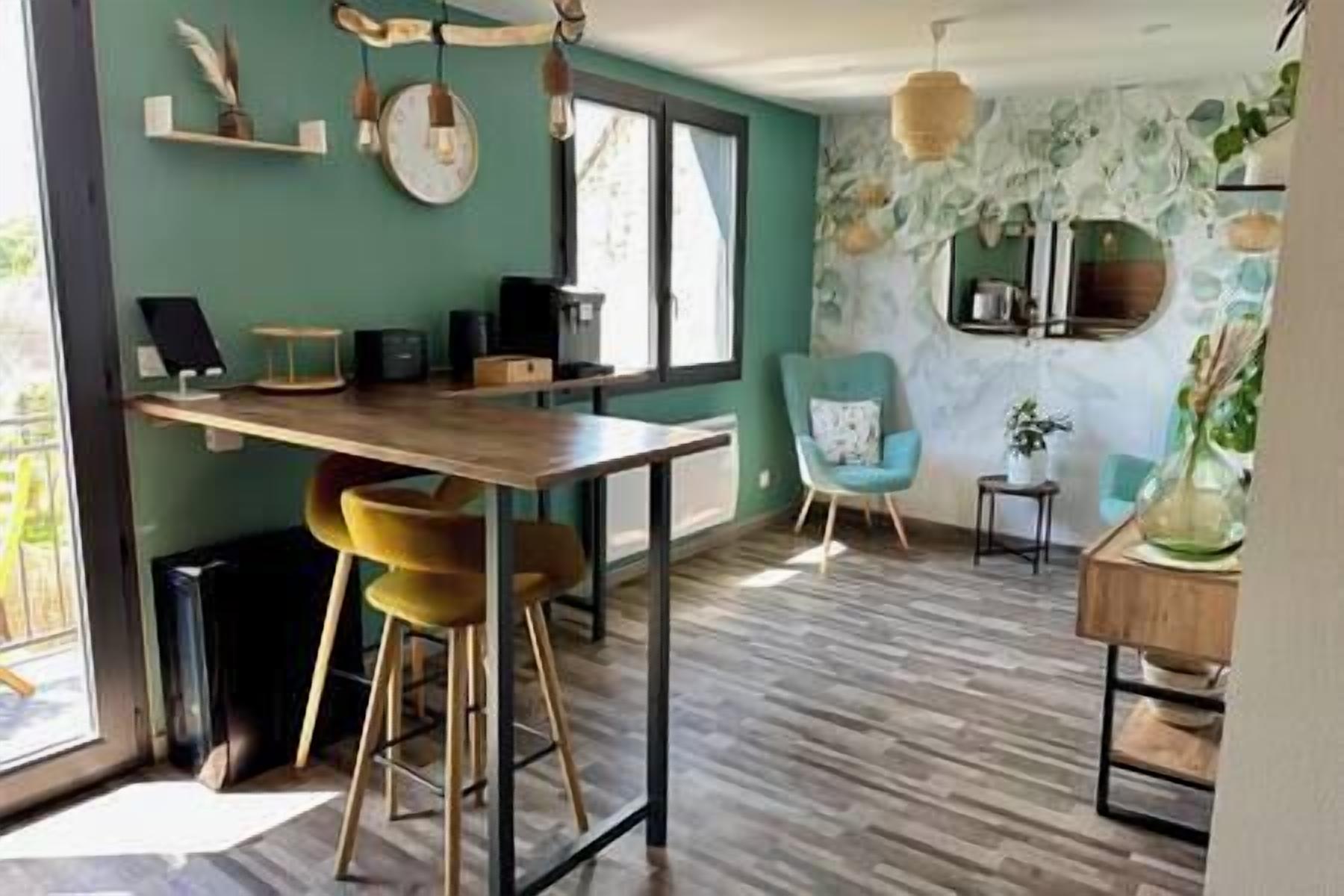 Une cuisine moderne avec une table en bois et des tabourets de bar, un fauteuil bleu et un mur en pierre agrémenté d’un miroir.