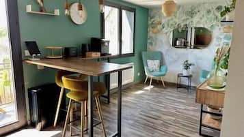 Une cuisine moderne avec une table en bois et des tabourets de bar, un fauteuil bleu et un mur en pierre agrémenté d’un miroir.
