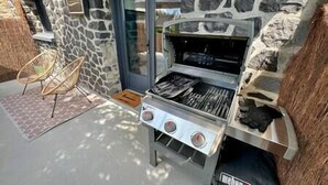 Ein Grillbereich im Freien mit einer Steinwand, einer Glastür und zwei Korbstühlen.