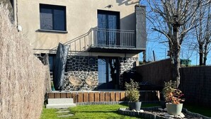 Ein zweistöckiges Haus mit einer Steinfassade, einer Holzterrasse und einem Kiesweg, der zum Eingang führt.