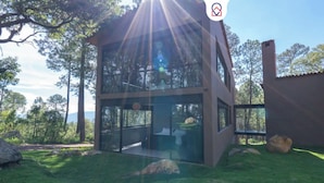 Ein modernes, zweistöckiges Haus mit großen Glasfenstern, einem Steinsschornstein und einem grasbewachsenen Garten mit Steinen.