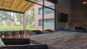 Ein modernes Schlafzimmer mit einem großen Bett, einem Fernseher und Blick ins Freie.