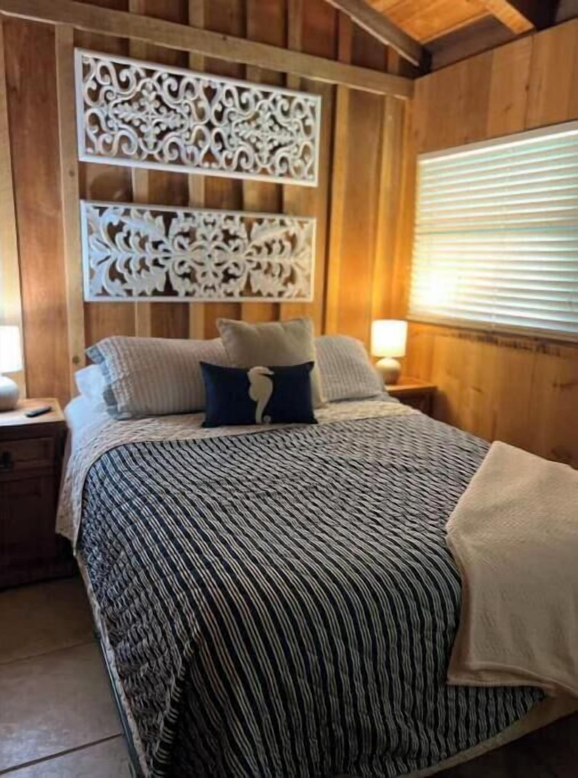 A wooden room with a bed, a decorative panel, and a window with blinds.