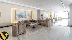 A spacious, modern living area with a sectional sofa, a coffee table, and a large abstract painting. - Vogue | Hera Tower Sports City near First Avenue Mall (Dubai)