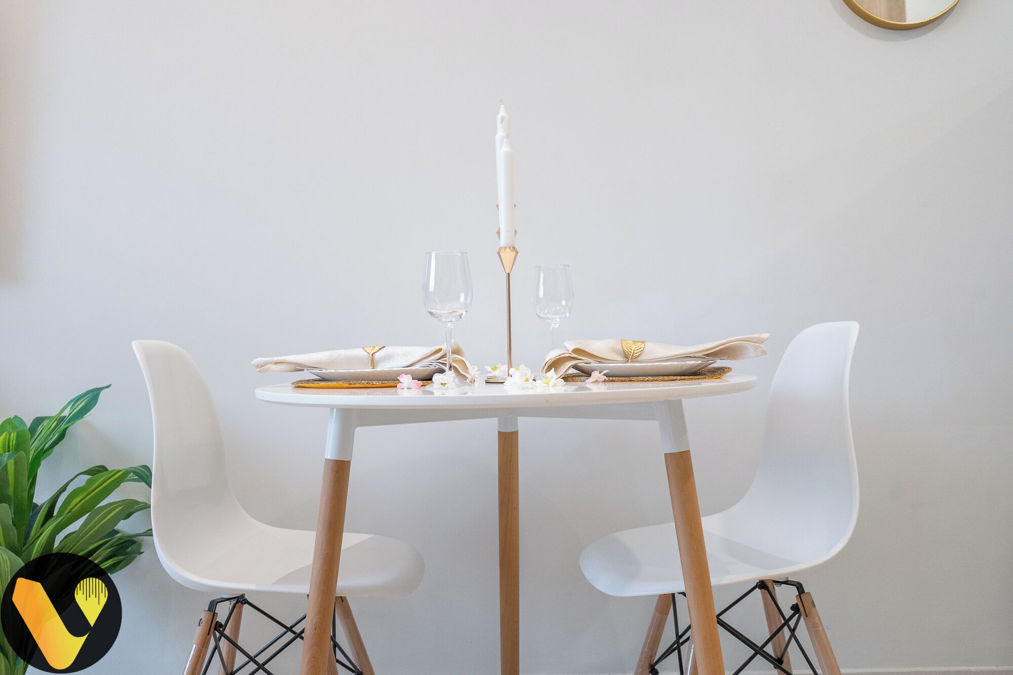 A dining table with white chairs, a white candle, and a gold decorative element on the table.