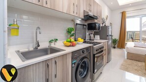 A modern kitchen with stainless steel appliances, a built-in washing machine, and a dining area with a view. - Vogue | Hera Tower Sports City near First Avenue Mall (Dubai)
