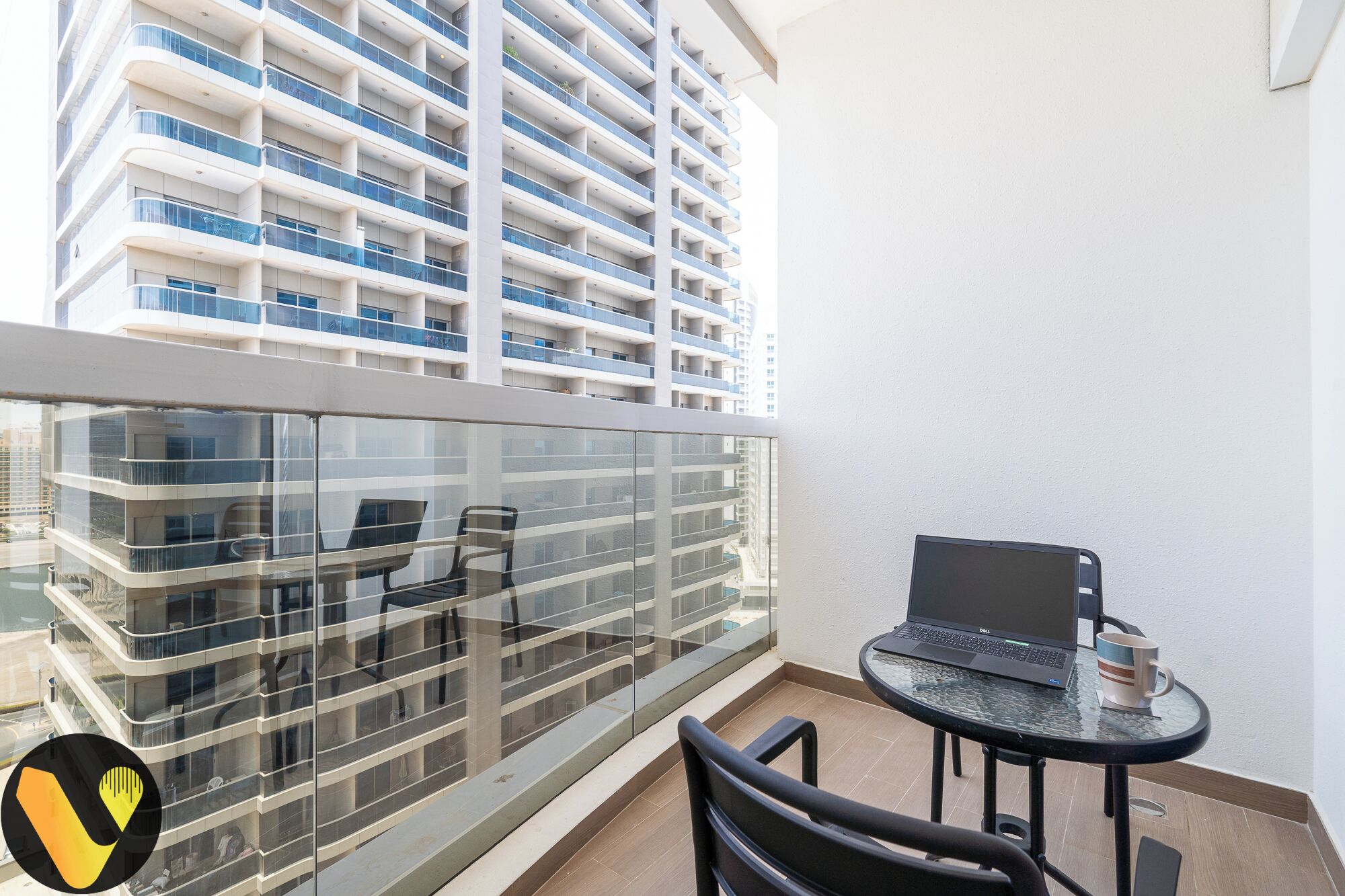 A balcony with a glass railing, a laptop on a small table, and two chairs.