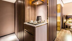 A modern hotel room with a wooden accent wall, a small kitchenette with a coffee maker, and a round table with a lamp. - Yinjiang PLUS Hotel (Hangzhou)