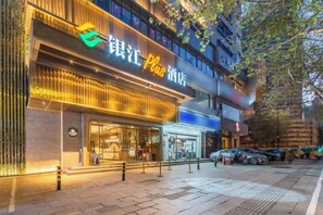 A hotel with a prominent sign, a visible entrance, and a parking area. - Yinjiang PLUS Hotel (Hangzhou)