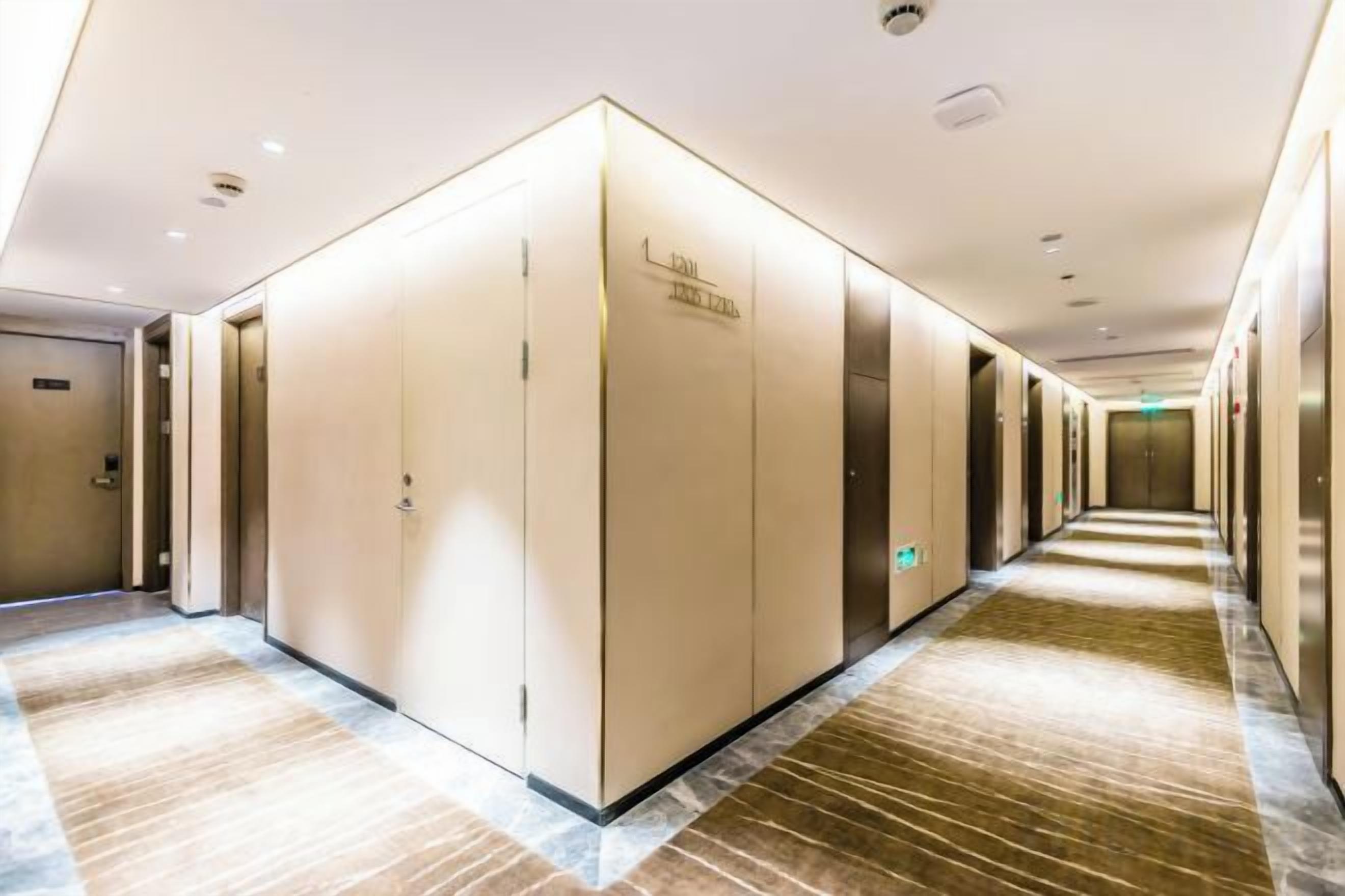 A hotel corridor with a central walkway, doors on both sides, and a carpeted floor.