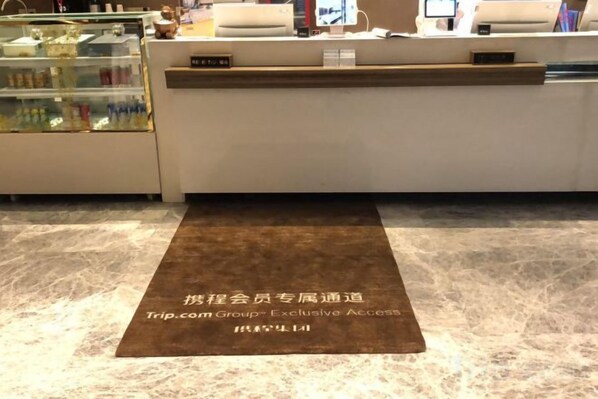 A reception area with a reception desk, a glass display case, and a brown mat with text. - Yinjiang PLUS Hotel (Hangzhou)