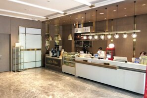 A modern reception area with a counter, glass display cases, and a coffee station. - Yinjiang PLUS Hotel (Hangzhou)
